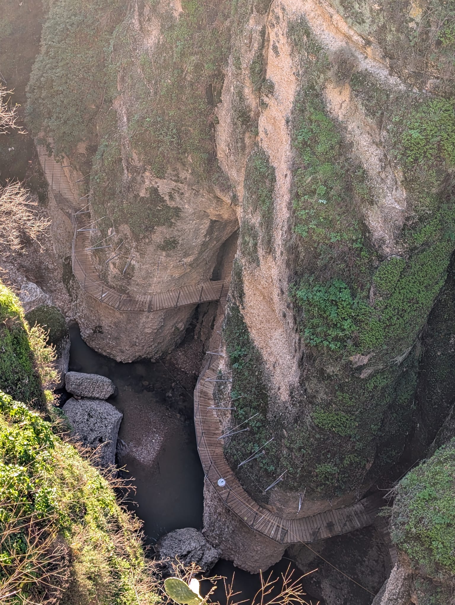 Je kijkt hier diep de kloof in, waar een smal houten wandelpad tegen de steile rotswanden is aangelegd. Dit pad slingert langs de rotsen en volgt de loop van het water beneden